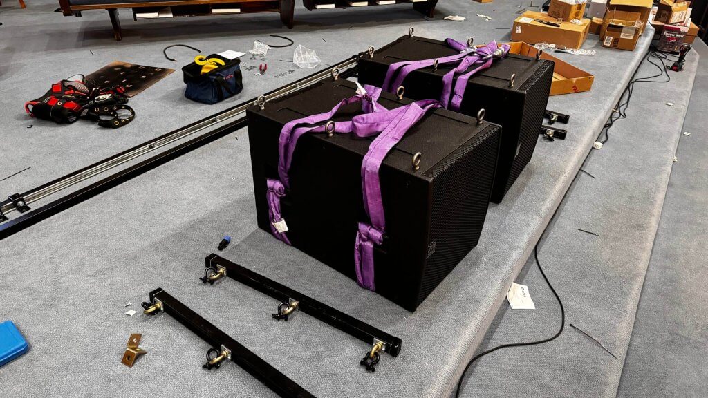 Interior, close-up view of two Martin Audio SXC115 cardioid subwoofers on church stage prepared with purple straps; these flown subs will create better church sound
