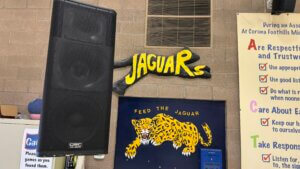 Middle school, interior, close-up shot of a tall three-way speaker next to the middle school mascot