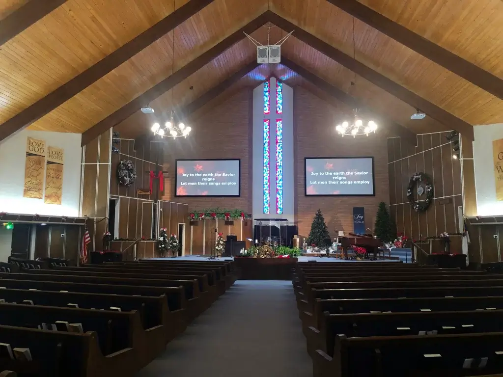 Interior, large sanctuary with two white speakers hanging from A-frame ceiling and two double 15-inch subwoofers past either side of the stage; this configuration produced poor church sound