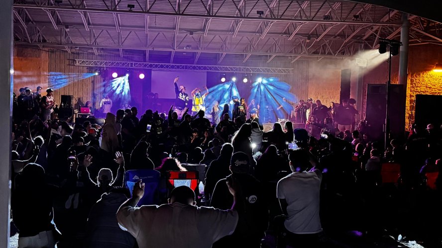 Large audience enjoying Christian hip-hop concert under professional stage lighting rental setup with colorful beams and atmospheric fog effects at Kennedy Park outdoor venue