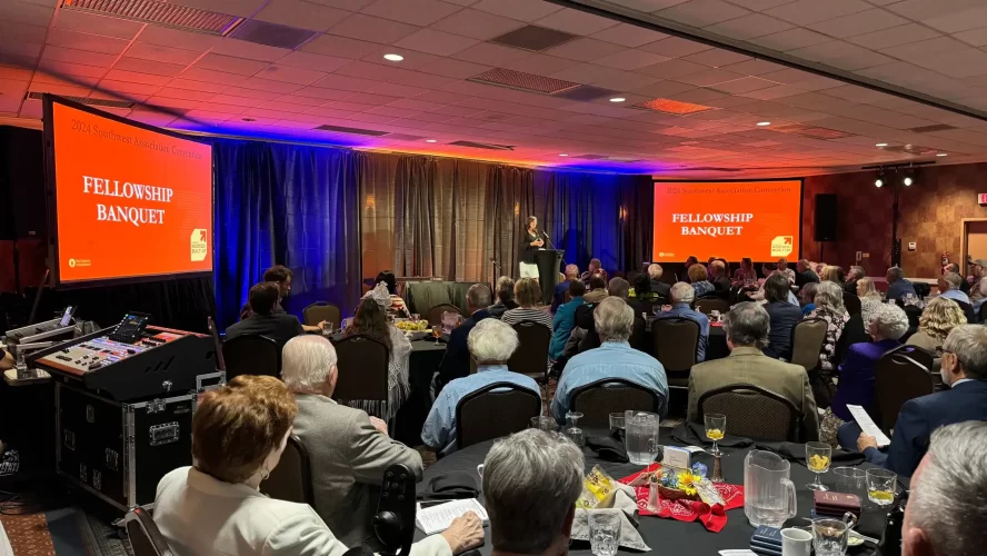 Audience seated at a banquet with audio visual equipment for events, including LED lighting, projector screens, and a Behringer Wing mixing console, at the Gideons' Southwest Association Convention Fellowship Banquet.