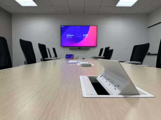 Conference room, interior, conference room AV solution featuring in-table charging station in the foreground, with several meetings chairs, tabletop microphones, and a colorful LED TV display with a soundbar camera in the background