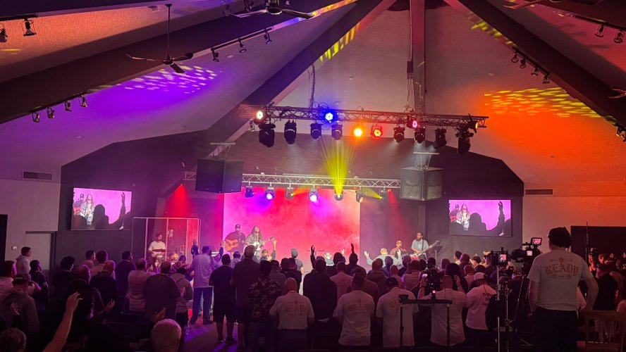 "Vibrant stage lighting rental setup at Christian worship concert with purple, orange and yellow beams illuminating band and engaged audience; when you rent lights for your event, new levels of worship are unlocked."